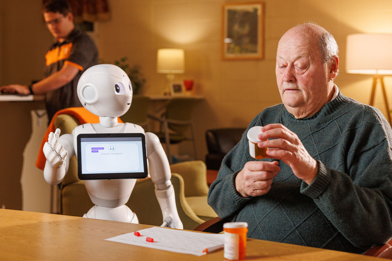 Patient interacting with medical assistance robot while a biomedical engineering PhD student takes notes in backgroun