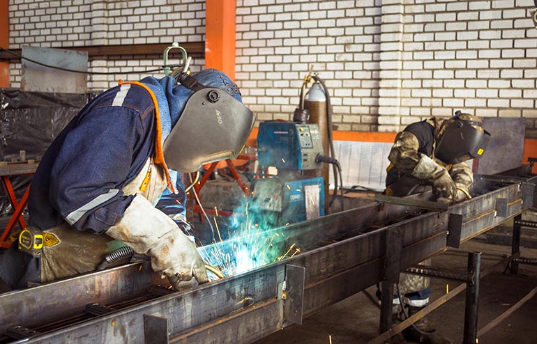 A student wearing a full compliment of safety gear welds in a workshop.