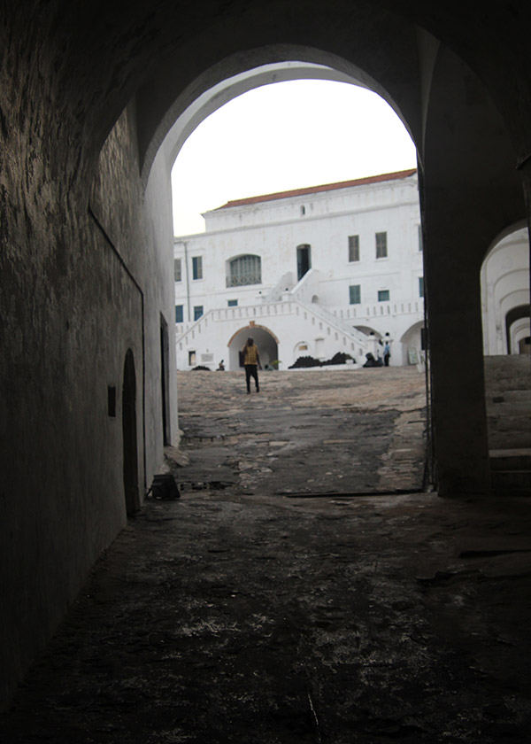 Large, white building beyond the entry to a dark dungeon.