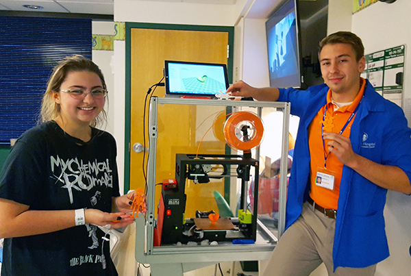 UT senior Brandon Rowell, right, a materials science and engineering major with a biomedical concentration, stands with East Tennessee Children's Hospital patient Shelby Layman and the 3D printer he has been taking around the facility.