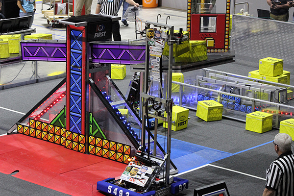 A competing robot stretches to place a block on the big scale.