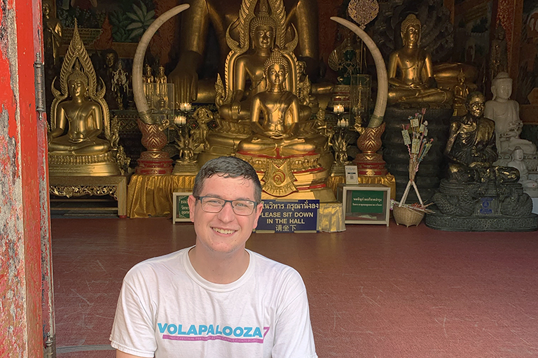 Caleb Moon sitting in front of Buddha statues.