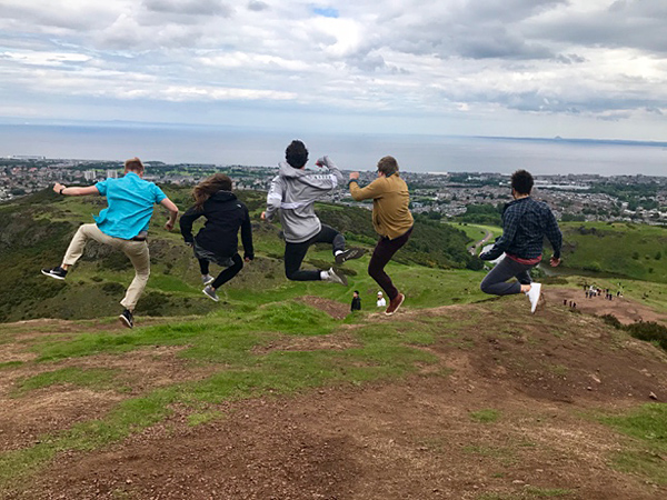Students jumping in a field overlooking a city.
