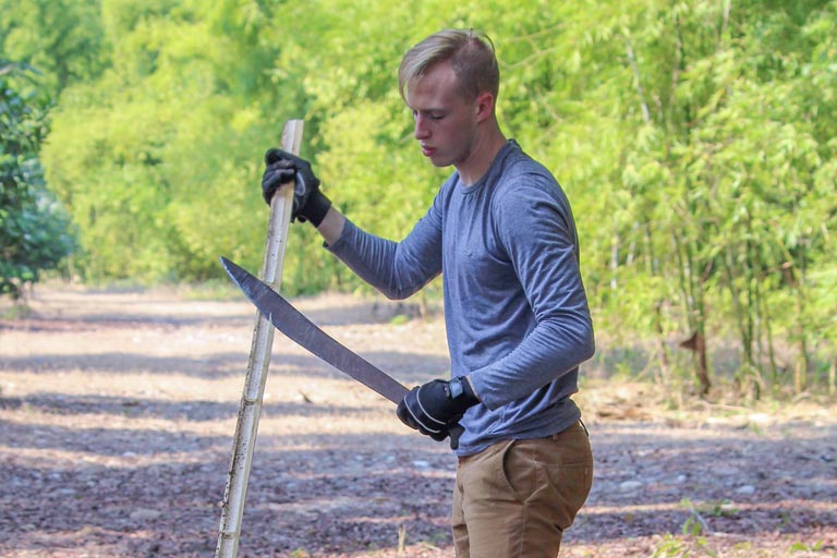 Tyler Wilcox trims bamboo with a machete