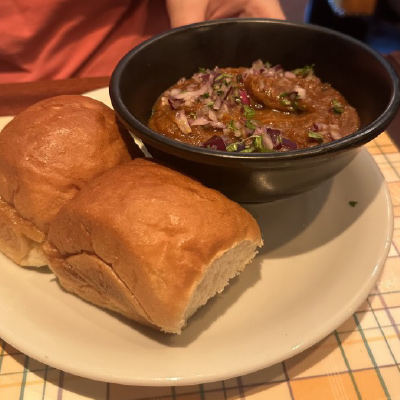 A meal of pav bhaji, rolls with spicy mashed vegetable filling, served on what appears to be a white ceramic plate, prepared inside of the famous London food markets.