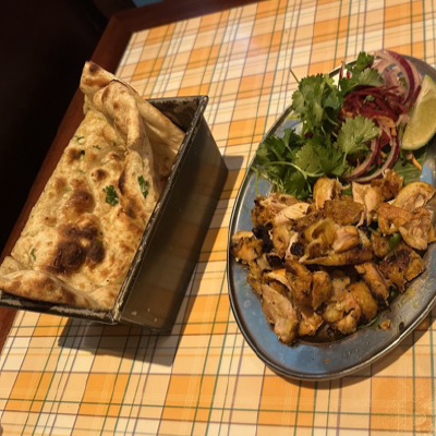 Chicken curry with a side salad garnished with a slice of lime on a plate, sitting on a table covered in a orange and white plaid tablecloth. Global cuisine prepared and served inside of the world famous London food markets.