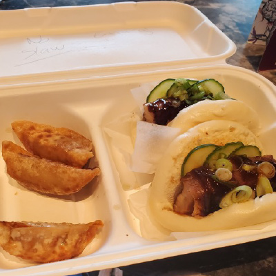 A meal of steamed buns garnished with pickles and green onion served inside of a styrofoam container from the world famous food markets in London, England.