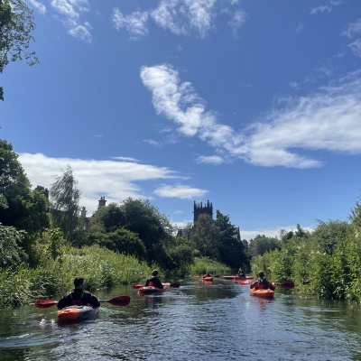 Austin Fisher and other Engineering in London study abroad group members kayak in a river that is highlighted by green foliage and plant life on either bank.