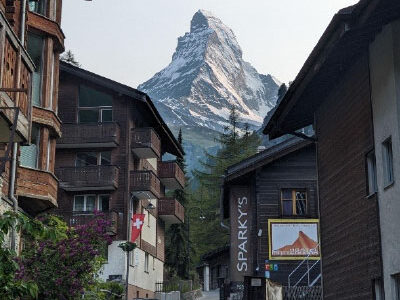A scenic view of Matterhorn, Zermatt. Resort and hotel-like buildings are shown in front of a snow-covered mountain.