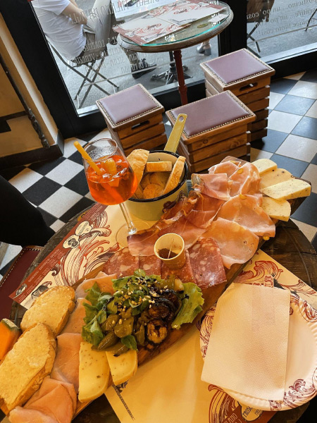 A large charcuterie board filled with assorted meats, cheeses, and bread. A drink in a long-stemmed glass sits to the side.