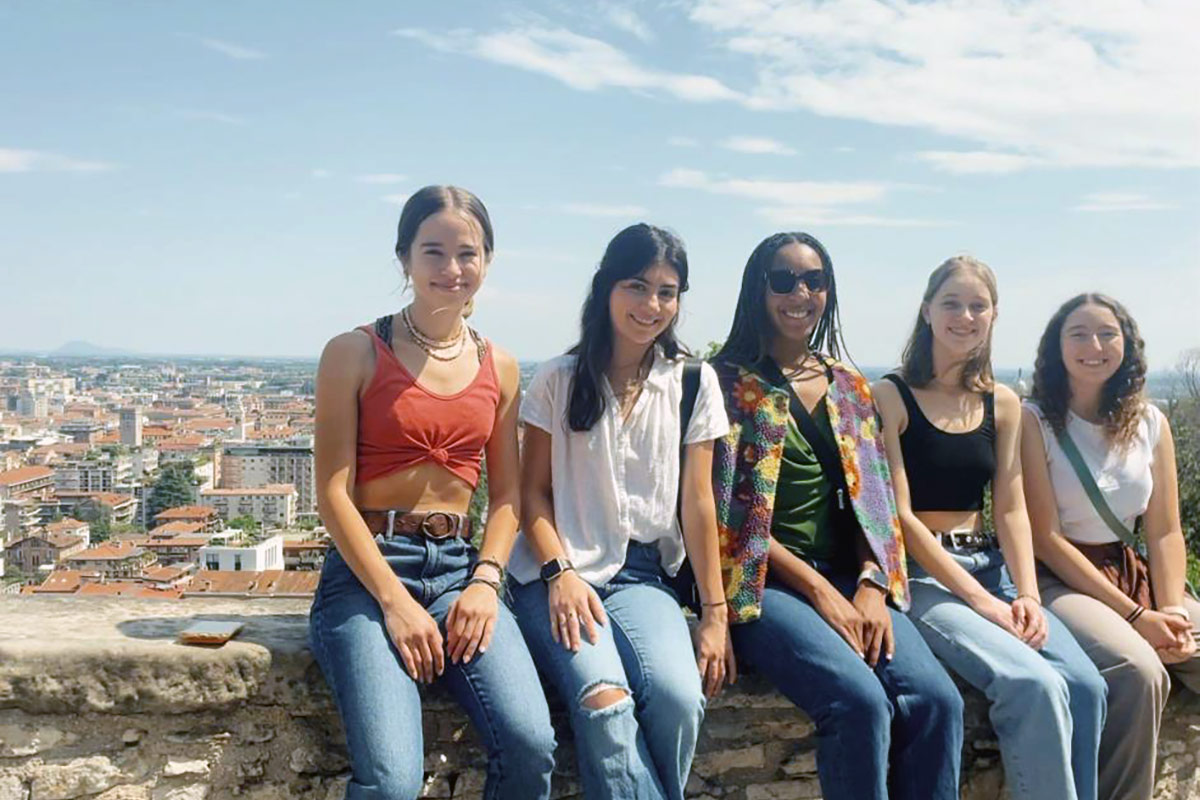 Haven Thompson and other study abroad participants sit together on a rock wall overlooking the city of Milan, Italy.