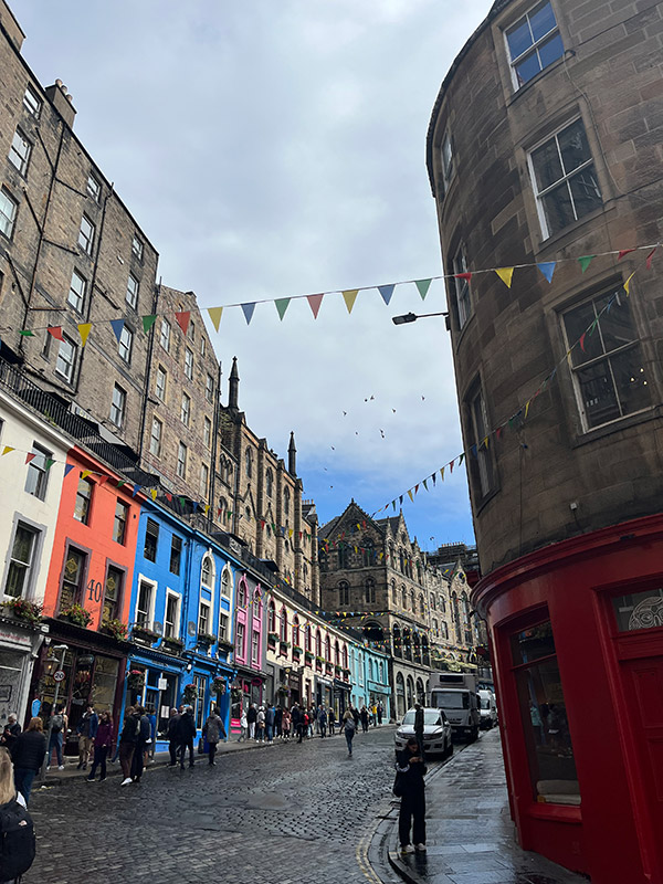 The Royal Mile in downtown London, England viewed from street level. Multiple buildings on the left side are painted in assorted colors from tan to red to blue to purple to tan to blue from nearest to furthest. A rounded top building stands on the front right side of the image with the bottom half painted red.