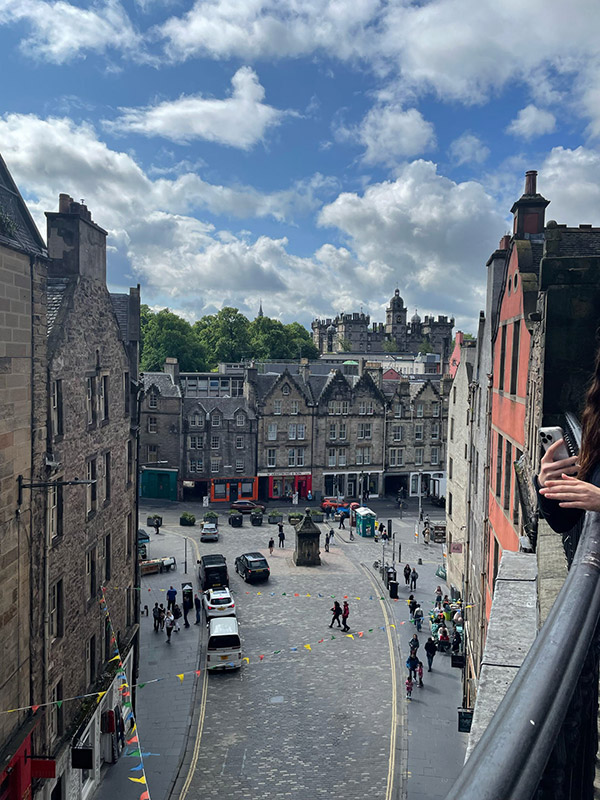 The Royal Mile is shown from an elevated view looking down from the top of a building. Multiple cars and people are on the street and sidewalk below.