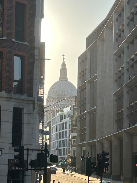 A view of the upper dome of St. Pauls Cathedral looking through an opening in between multiple high-rise buildings in a downtown scene.