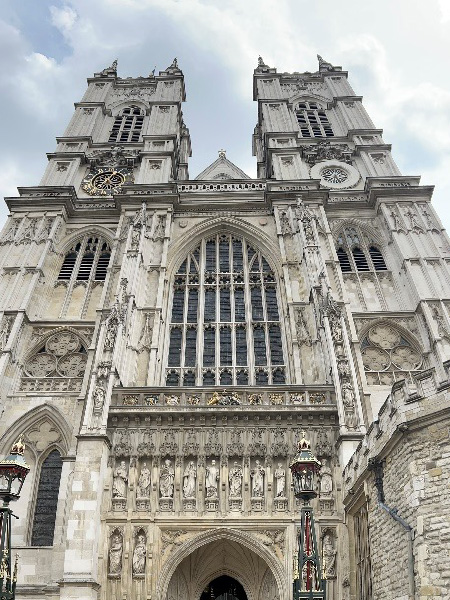 A view of the exterior of Westminster Abbey in London, England. The building is a tan-like gray that features aged ornamental decorations and bricks. 