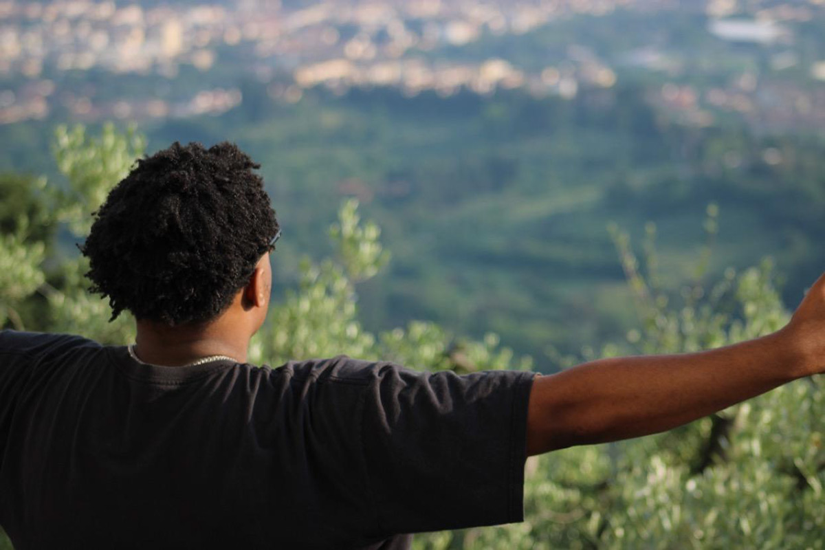 Stephen Walker Jr. stands with his arms extended and his back to the camera at an elevated location overlooking Florence, Italy. The view consists of a large valley covered with trees and the outskirts of the city.