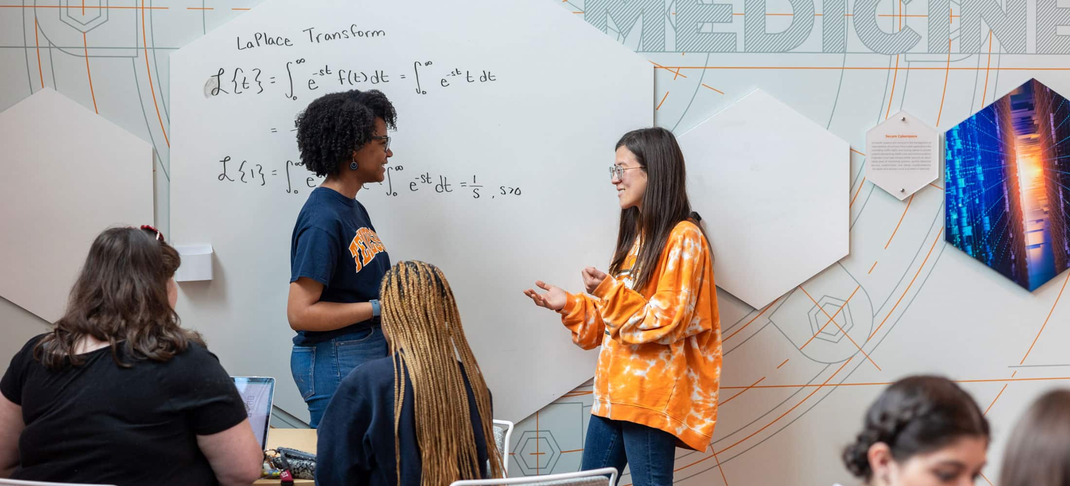 Two women in engineering talking at a whiteboard in a classroom