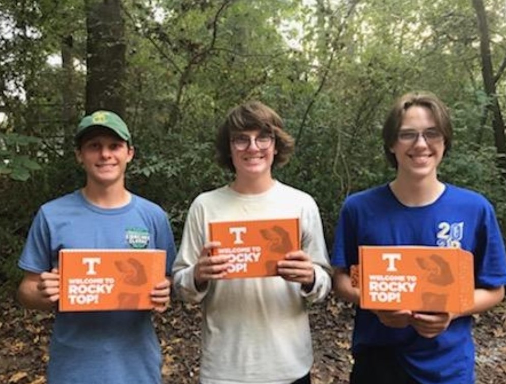Walker, Jackson, and Grey Reeves standing in the woods holding their UT acceptance boxes
