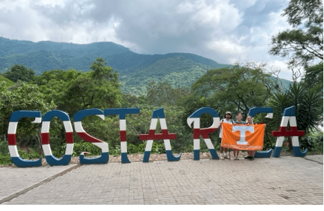 Rebecca Mozingo holding a University of Tennessee flag standing next to letters that spell "Costa Rica"
