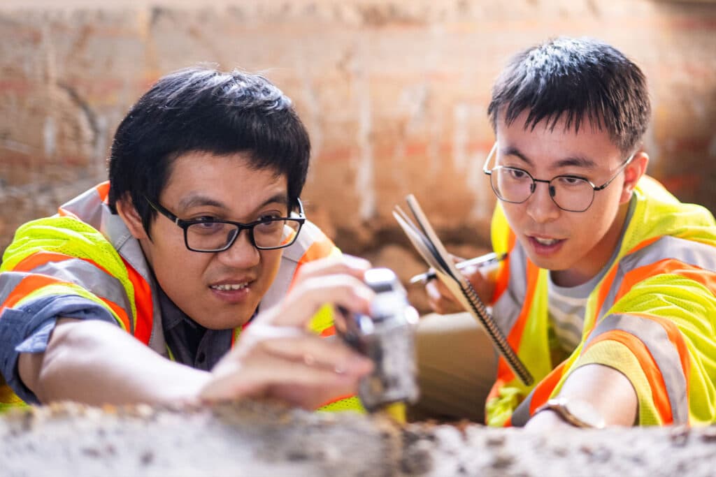 Graduate student Jingtao Zhong measures the layers in an experimental road surface while Assistant Research Professor Yuetan Ma observes and records data following testing in the high bay lab in the John D. Tickle Engineering Building.
