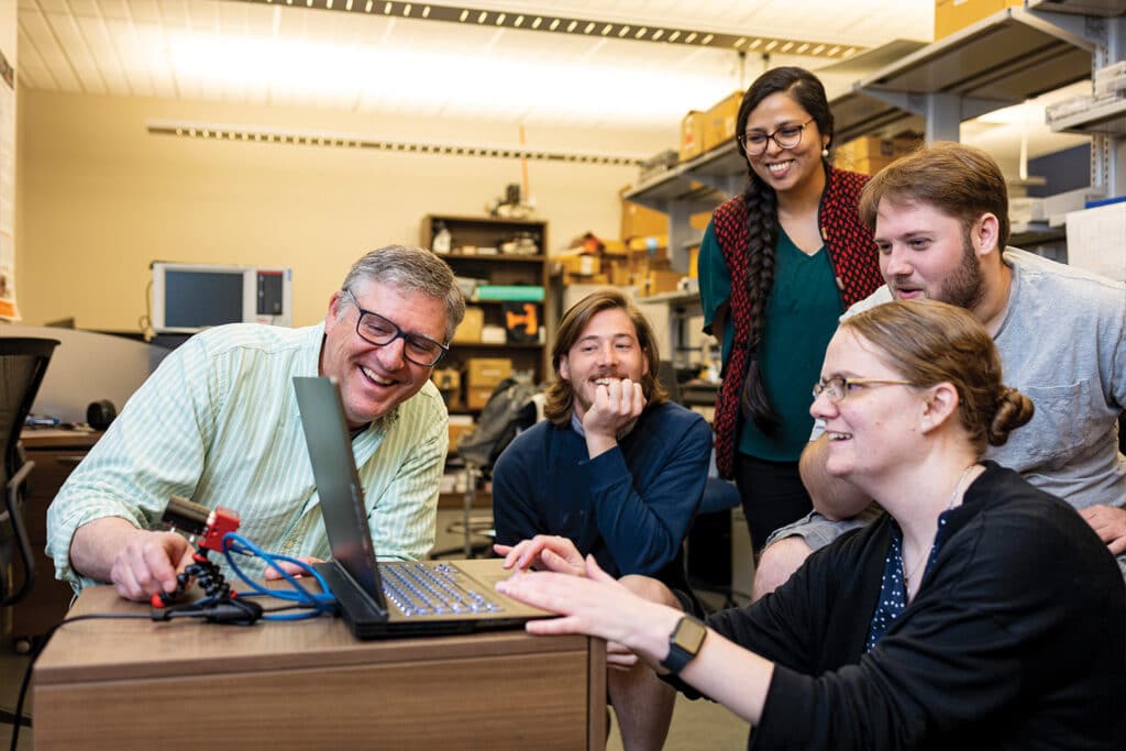 Graduate students work on a computer with faculty members James Plank and Catherine Schuman