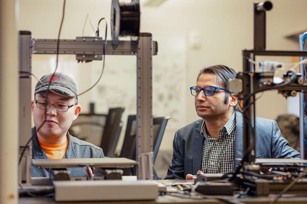 Student works on 3D printer with Associate Professor Himanshu Thapliyal in a Min Kao Engineering Building lab.
