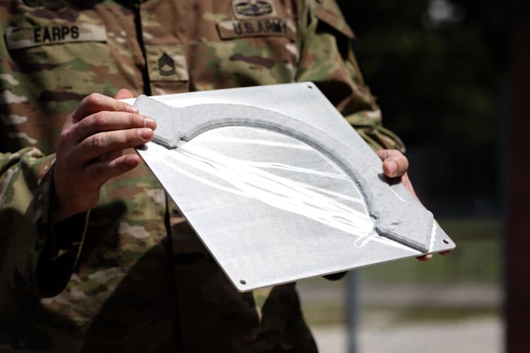 Army soldier shows printed and repaired part for a Bradley Fighting Vehicle