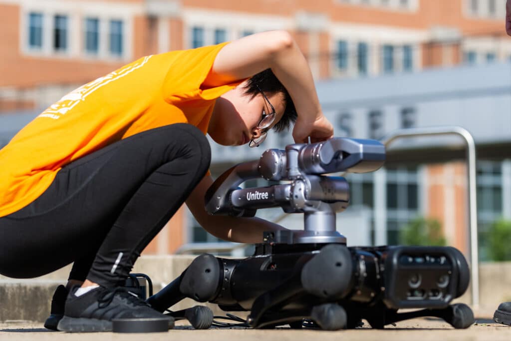Graduate students Mengjun Wang and Ning Hu remove an installed arm from a robot dog as part of their research at the Gate 21 amphitheater.