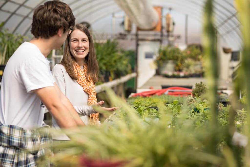 Kelsey Ellis pretends to work with a student during a Volunteer Story photoshoot inside a greenhouse on the AG Campus