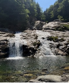 Waterfall cascading down rocks with pine trees behind it