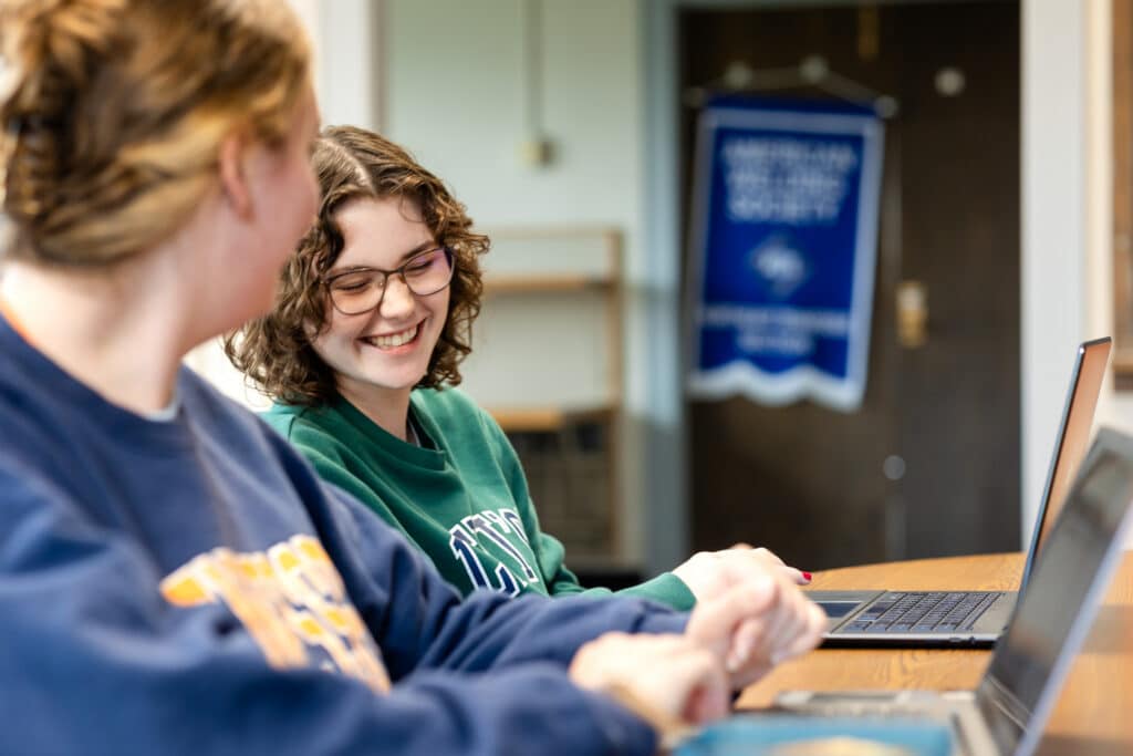 Two female students smiling at their computer screens together