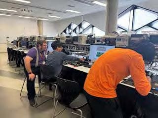 Novus and classmates working in a soldering lab with a Sheffield Technician.