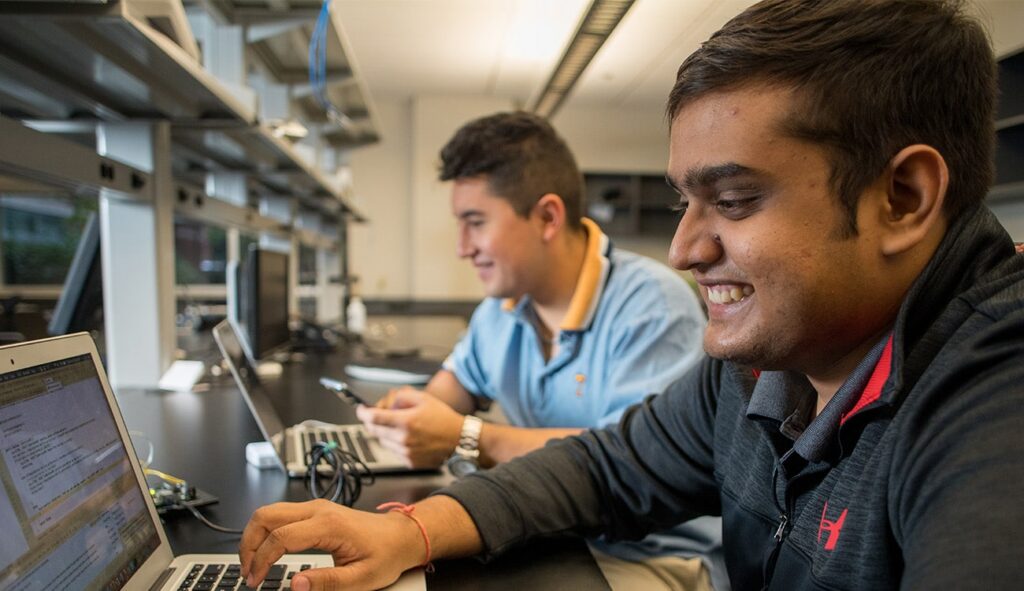 Students smiling while looking at their laptops in a lab