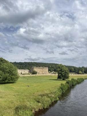 Distant view of Chatsworth House with lush green grass and a river in the foreground